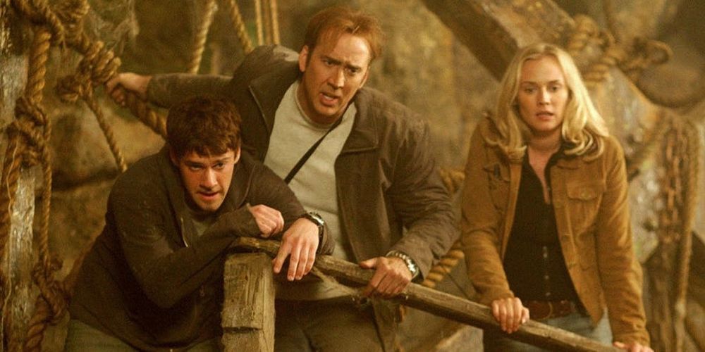 Benjamin, Riley y Abigail miran por encima de una barandilla hacia una caverna en National Treasure.